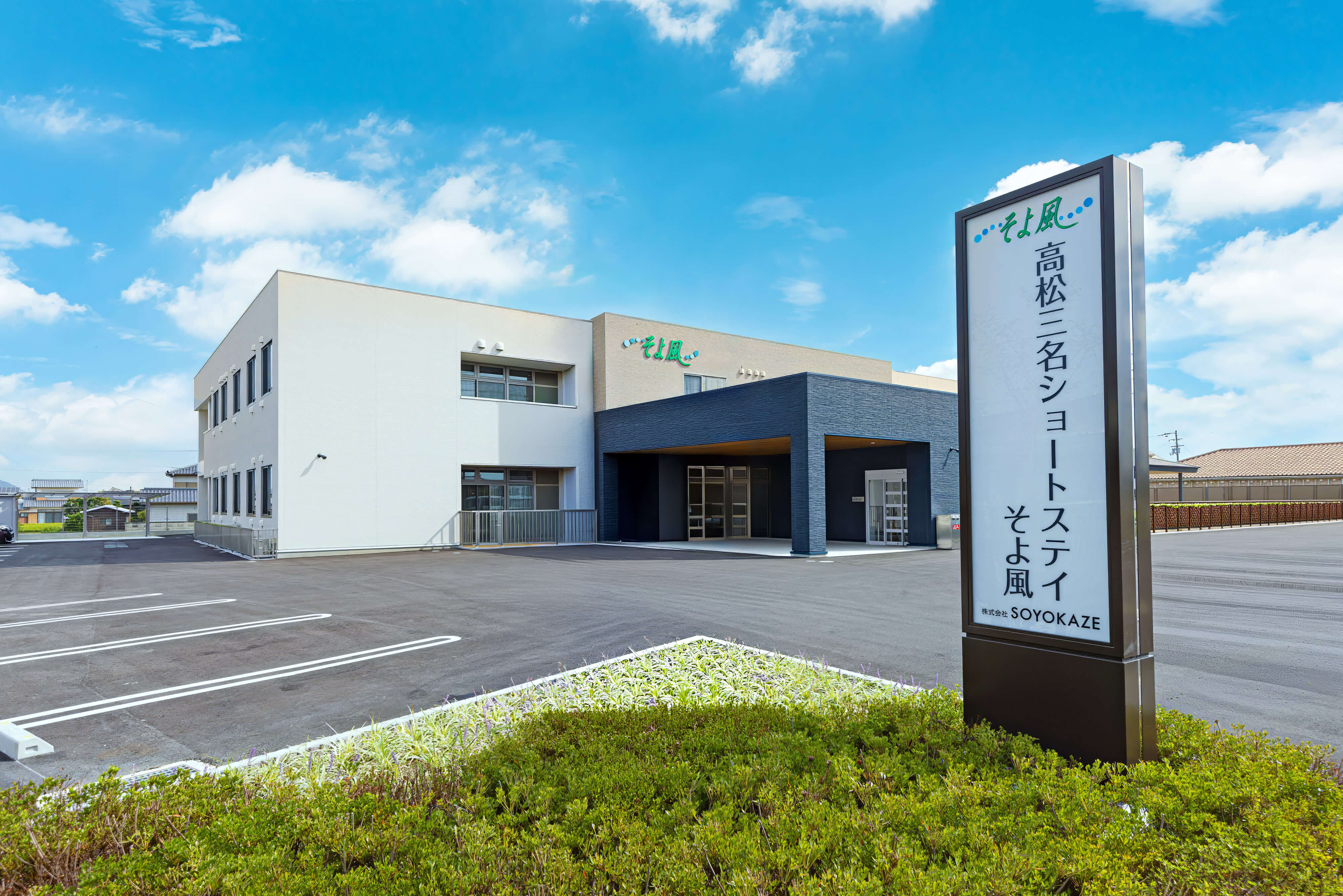 介護施設の建物外観。白と黒の現代的な建築で、敷地内に案内看板が立っている。